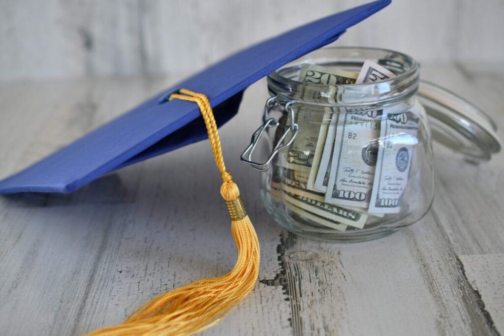 education costs concept a graduation cap mortarboard and tassel next to a jar of dollar bills