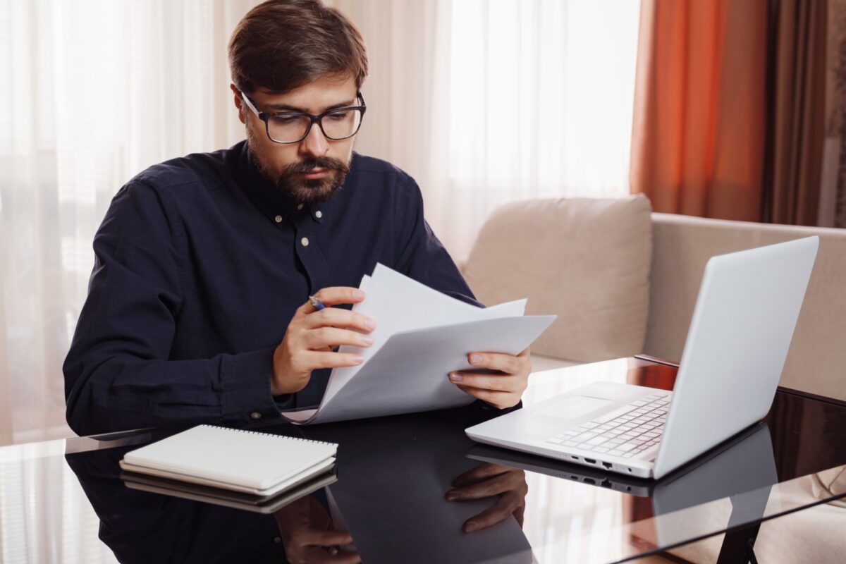 entrepreneur in eyeglasses works with a laptop and reviews documents